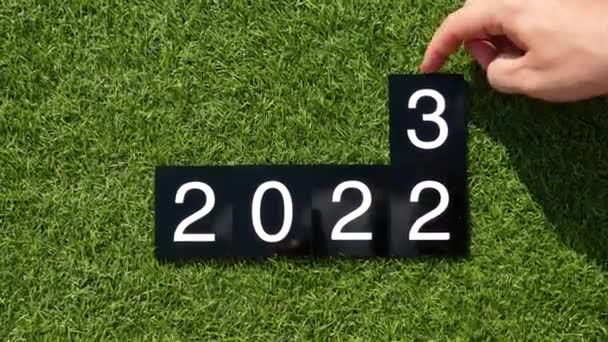 2023年あけましておめでとうございます 2022 2023年変更 人間の手は緑色の芝生の上で2022年から2023年までの数字でプラスチック板を変え 2番を削除します さようなら2022 2023へのこんにちは 介護環境の概念 — ストック動画