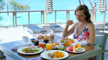 Happy woman eat breakfast or brunch in luxury outdoors restaurant at tropical hotel in sunny summer day, blue sea background. Travel to Thailand, holiday or vacation on Phuket, female tourist concept.