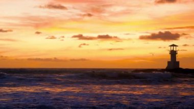 Scenic view of surf people sitting with surfboards in ocean water waves on sunset. Tropical beach with lighthouse on background. Concept of travel, adventure and sporty time