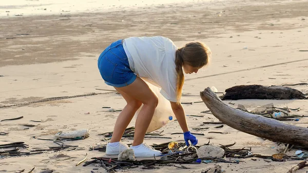 Woman volunteer collect trash from the sea beach in a trash bag. Plastic pollution and environmental problem concept. Cleaning ocean from pollution. Green planet.