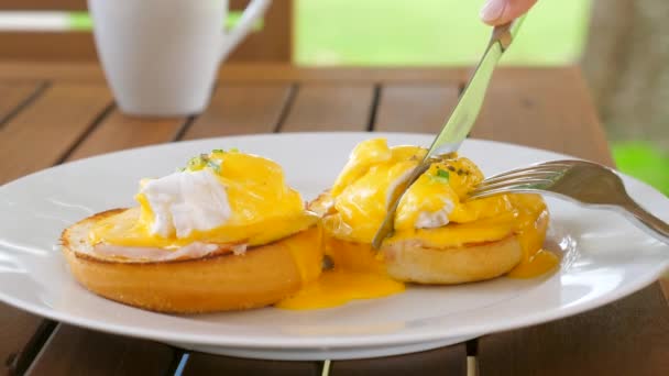 健康早餐食品 餐馆里的烤面包 盘子里放着煮过的鸡蛋 女人吃美味的鸡蛋本尼迪克特与全麦酱 雌性手在里面用液体蛋黄切鸡蛋 靠近点 — 图库视频影像