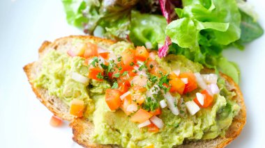 Sağlıklı tost, parçalanmış avokado, doğranmış domates ve beyaz tabakta soğan ve bahçe salatasıyla yakından bakın. Sağlıklı vejetaryen yemeği kavramı