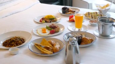 Yatakta kahvaltı, rahat bir otel odası. Tatil kavramı, lüks otellerde tatil. Otel restoranında taze yemek siparişi, oda servisi. Yumurtalı lezzetli yemekler, pastırma, makarna ve portakal suyu.