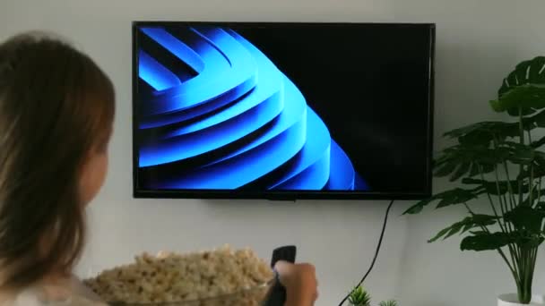 女人拿着电视遥控器 拿着一碗爆米花在屏幕上观看Amazon Prime Video应用程序 坐在沙发上的女性在电视前 屏幕上有亚马逊总理的标志 2022年9月 泰国普吉 — 图库视频影像