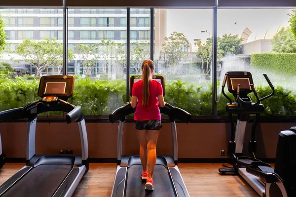 Young woman running on treadmill. Fitness girl in sportswear doing cardio exercise, walking on treadmill in modern gym. Back view. Active lifestyle, healthy concept