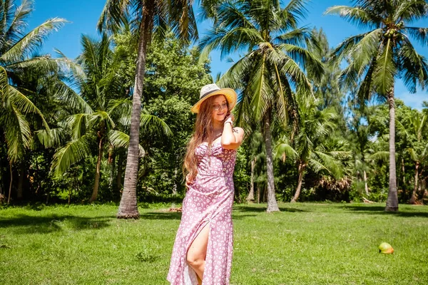Travel happy woman in straw hat and dress relaxing on summer vacation on tropical paradise island among coconut palm trees. Happy traveller woman enjoys her Thailand exotic trip. Wanderlust concept