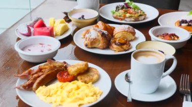 Restoranda kahvaltı. Taze hamur işleri, meyveler, omlet, tost, yoğurt ve ahşap masada bir fincan kahve. Otelde günaydın.