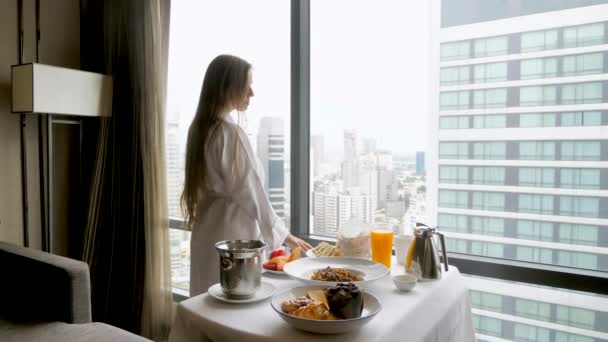 女人在豪华酒店吃早餐 穿着浴衣的旅行女孩享受着窗外的美景 度假时放松一下 现代公寓的客房服务或浪漫惊喜 — 图库视频影像