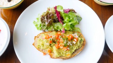 Kafede sağlıklı vejetaryen kahvaltısı. Avokado tostu, avokado püresi, doğranmış domates ve yeşil salatalı taze soğan. Uygun vejetaryen yemeği kavramı. Üst görünüm
