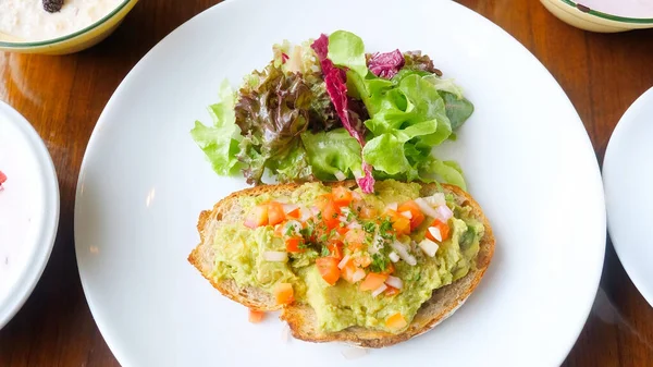 Kafede sağlıklı vejetaryen kahvaltısı. Avokado tostu, avokado püresi, doğranmış domates ve yeşil salatalı taze soğan. Uygun vejetaryen yemeği kavramı. Üst görünüm