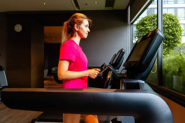 Young woman running on treadmill. Fitness girl in sportswear doing cardio exercise, walking on treadmill in modern gym. Active lifestyle, healthy concept