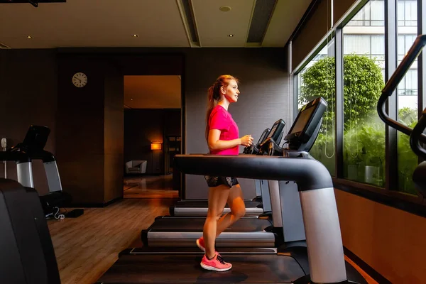 Young woman running on treadmill. Fitness girl in sportswear doing cardio exercise, walking on treadmill in modern gym. Active lifestyle, healthy concept