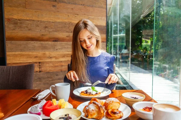 Attractive woman on brunch in hotel buffet restaurant. Female person on dine in modern cafe, drinking coffee. Table full of healthy food and beverage.