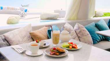 Açık hava kafeteryasında deniz manzaralı kahvaltı servisi yapmış. Bir bardak buzlu kahve, bir fincan sıcak çay, Belçika waffle 'ı, krep, tropikal meyveli bir tabak. Otel tatlı öğle yemeği ya da kahvaltı. Deniz tatil beldesinde tatil