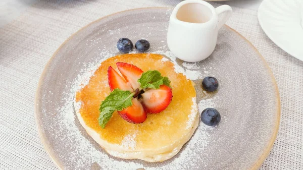Delicious buttermilk pancake with fresh berries and maple syrup in small jug. Tasty sweet food on breakfast in hotel or cafe. Dessert with strawberry and blueberry.