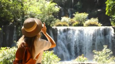 Tayland 'da tropikal tatil yapan tanınmamış bir gezgin kadın. Asyalı şelalede fotoğraf makinesi olan kadın blogcu. Yaz yolculuğu, seyahat tutkusu konsepti. Yavaş çekim