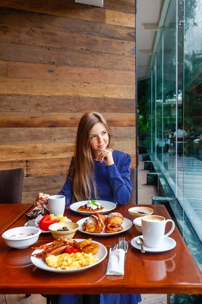 Attractive woman on brunch in hotel buffet restaurant. Female person on dine in modern cafe, drinking coffee. Table full of healthy food and beverage.