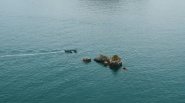 Turkuaz denizde tahta tekne, mavi sudaki tropik kayaların yakınında hareket. Turistlerle dolu bir gezi teknesi temiz mavi deniz yüzeyinde yüzüyor. Okyanusta küçük dalgalı bir tekne. Seyahat, tur, turizm kavramı.