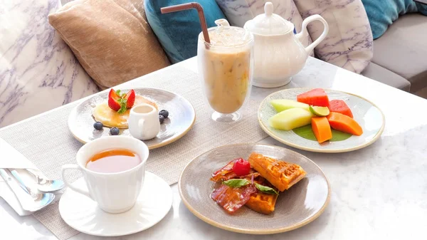 Sweet delicious breakfast with pancake, waffles, coffee and fresh fruits. Breakfast table in hotel. Morning food in cafe. Dessert meal with pastry, tea and cappuccino