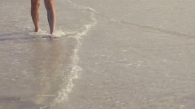 Gün batımında deniz kıyısında yalınayak yürüyen bir adam. Tayland, Phuket 'te yaz tatilindeki erkek turist. İnsan bacakları ve ayakları kumlu sahilde tek başına okyanusta su dalgalarında yürüyor..