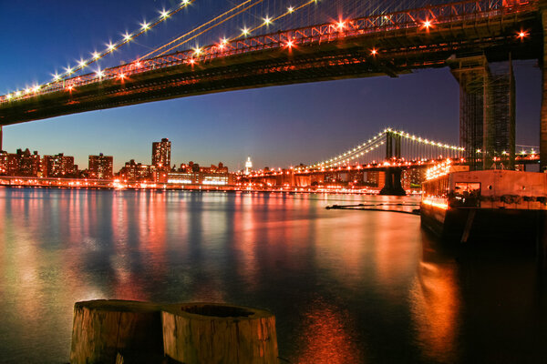 New York City Manhattan skyline with Brooklyn Bridge and office skyscrapers building in at dusk illuminated with lights at night