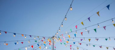 Mavi gökyüzü üzerinde renkli flama ve ampullerle süslenmiş çelenkler. Uzun biçim