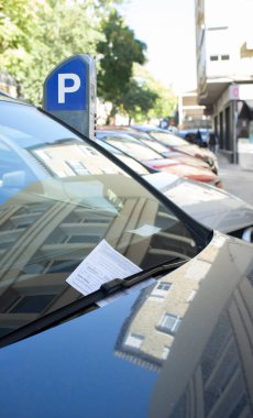 Vehicle fined for having parked in the blue zone. Ticket under the windshield wiper with parking meter at the bottom clipart