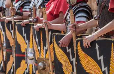 Roman legionaries in formation. Hands holding pila or javelins. Faint eagle-wing and thunderbolt motifs on the scuta clipart