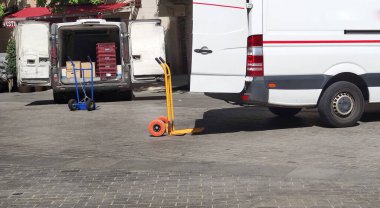 Vans unloading food at downtown. There is a cart beside each vehicle
