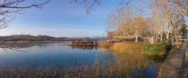 People enjoying the winter sun over pier restaurant at  Lake of Banyoles, Girona, Catalonia, Spain