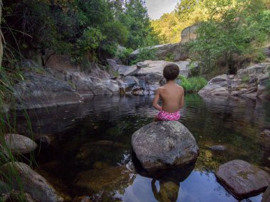 Child boy sitting at upriver swimming pool of Vadillo Gorge. Losar de la Vera, Caceres, Extremadura, Spain