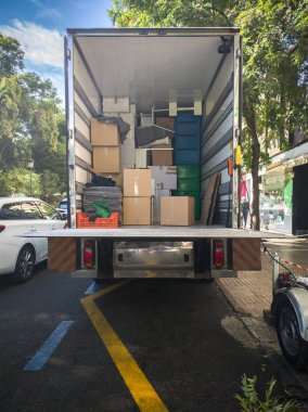 Yarı karavan nakliye kamyonu şehir merkezindeki caddede malları yüklüyor. Asansör rampasıyla donatılmış.