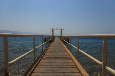 Mavi denize uzanan ahşap güverteli demir köprü
