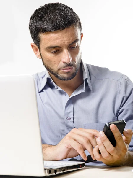 Jeune homme avec barbe travaillant sur ordinateur portable et téléphone portable — Photo