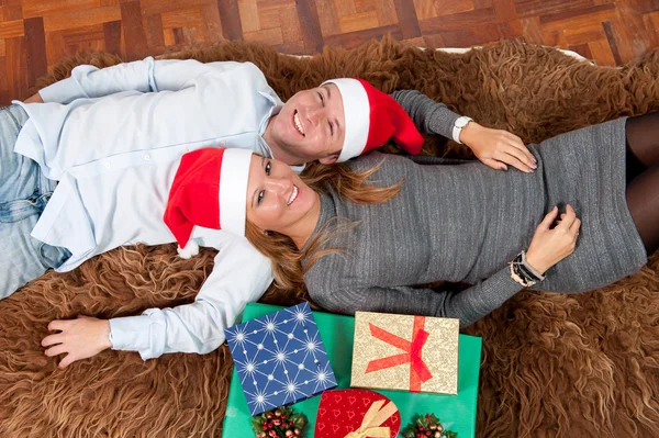 Unga lyckliga paret med presenterar på matta på jul — Stockfoto