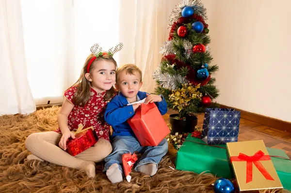 Kleine Kinder auf Teppich öffnen Weihnachtsgeschenke — Stockfoto