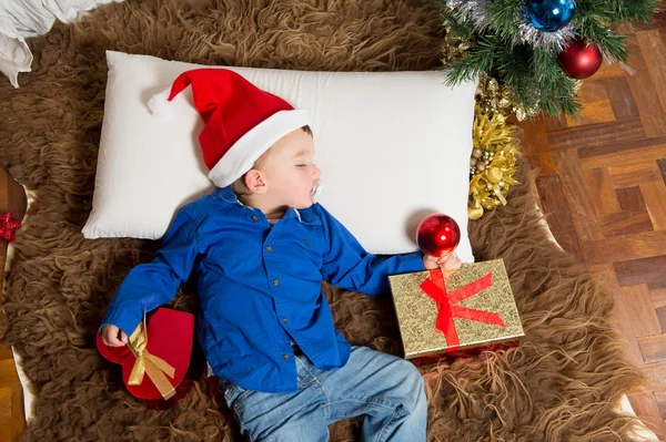 Noel Baba şapkalı halının üstünde uyuyan sevimli küçük çocuk — Stok fotoğraf