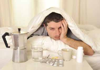 Man with headache and hangover in bed with tablets clipart