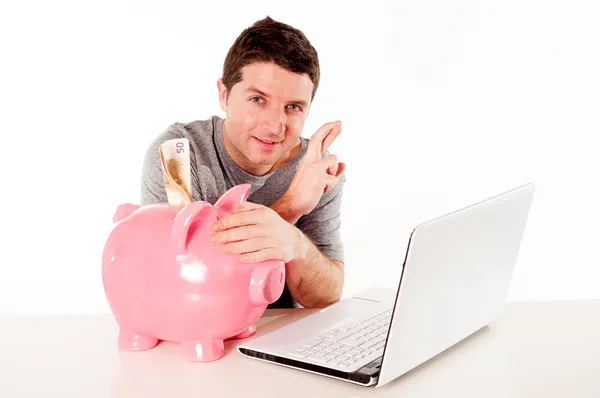 Homem com banco porquinho e laptop pensando em salvar on-line — Fotografia de Stock