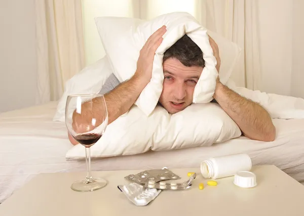 Hombre con dolor de cabeza y resaca en la cama con tabletas — Foto de Stock