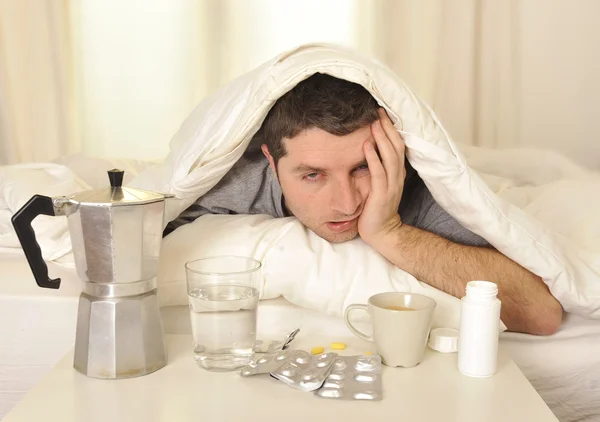 Hombre con dolor de cabeza y resaca en la cama con tabletas — Foto de Stock