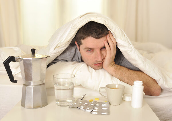 Мужчина с головной болью и похмельем в постели с таблетками
