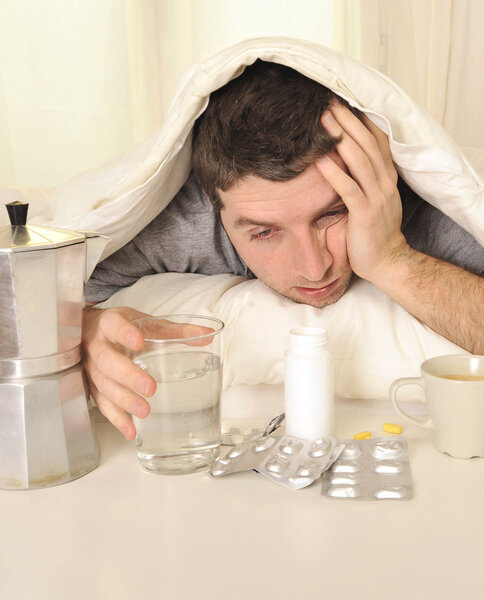Man with headache and hangover in bed with tablets