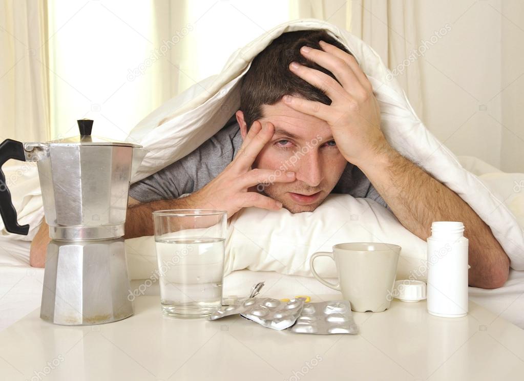 Man with headache and hangover in bed with tablets
