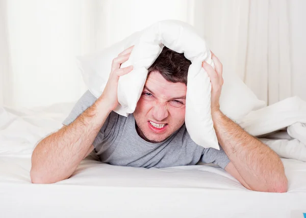 Мужчина страдает похмельем и головной болью с подушкой на голове — стоковое фото