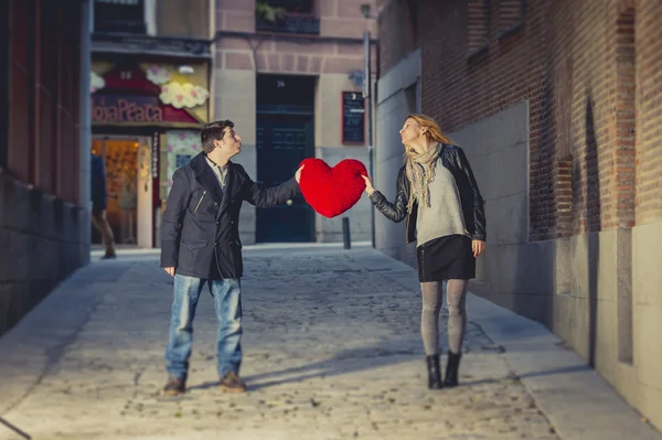 Attractive couple kissing with a red heart pillow — Stock Photo, Image