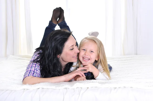 Gelukkig jonge moeder met schattig dochtertje glimlachen op bed — Stockfoto