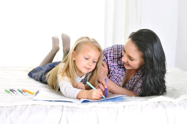 Young Mother and beautiful little daughter lying and drawing together — Stock Photo, Image