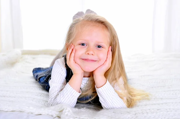 Adorable blonde blue eyed little girl lying happy on bed — Stock Photo, Image