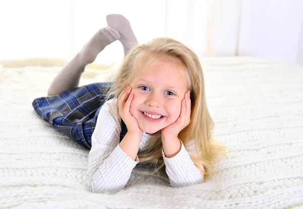 Entzückendes blondes blauäugiges kleines Mädchen liegt glücklich auf dem Bett — Stockfoto